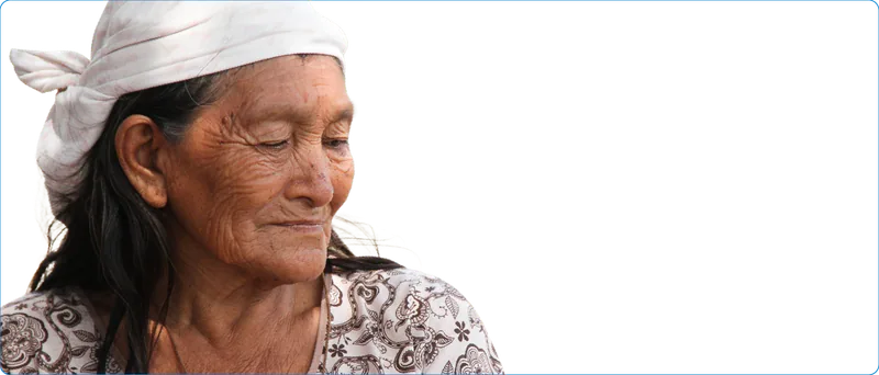 Mujer campesina mayor con pañuelo blanco en la cabeza y blusa estampada, con la mirada baja.