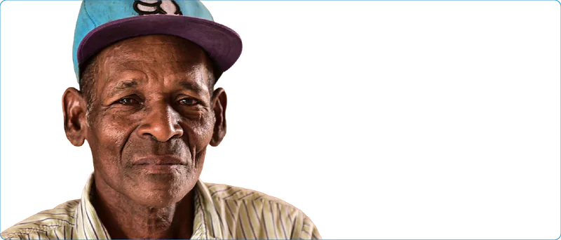 Hombre afrodescendiente mayor con gorra azul y camisa de rayas.