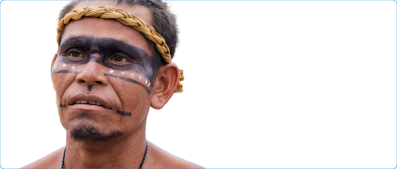 Hombre indígena con corona de fibra trenzada y pintura facial, mirando al horizonte.