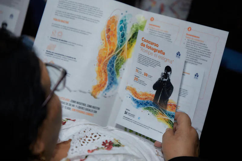 Una asistente al lanzamiento lee el folleto de la campaña, abierto por la página del concurso de fotografía «Rompe el estigma».