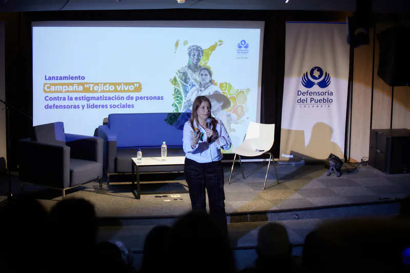Una mujer interviene con micrófono en el escenario durante el lanzamiento de la campaña Tejido vivo contra la estigmatización de personas defensoras y líderes sociales.